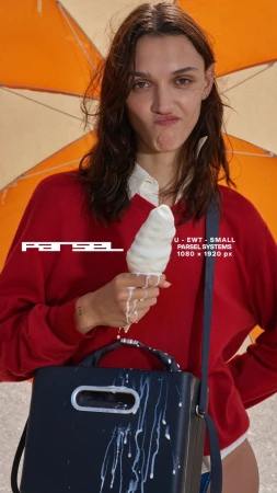 Woman in red sweater enjoys melting ice cream cone by orange umbrella, posing with navy lunchbox bag on outdoor surface.