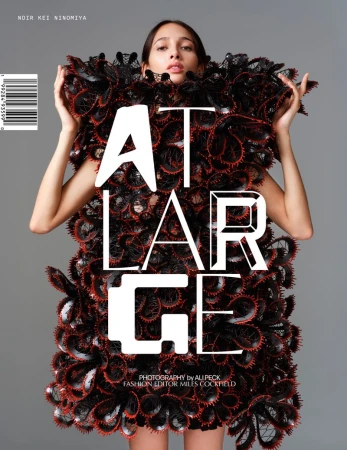Fashion editorial shot of an adult female model wearing a black sculptural dress standing in front of a grey studio background with text overlay.