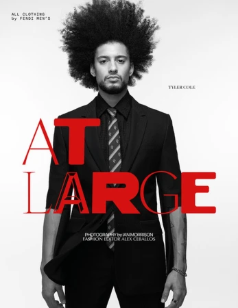 An adult male with an afro poses in a black suit with a tie, against a bright background with red overlaid text for a fashion editorial.