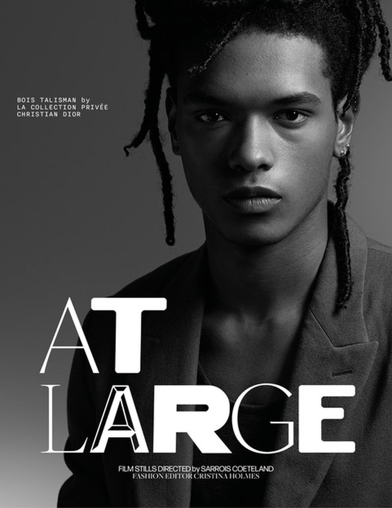 Portrait of a Black male fashion model with dreadlocks wearing a blazer in a studio with gray background and graphic design overlay.