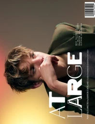 A young man wearing a green blazer rests his hand near his chin against a gradient background for At Large Magazine.
