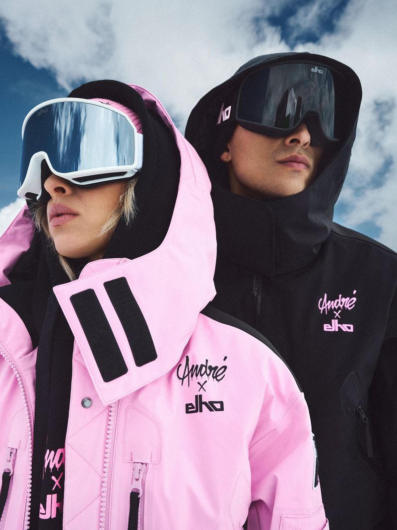 Two fashion models in ski jackets and goggles pose against a cloudy sky, showcasing winter sports and outdoor apparel.