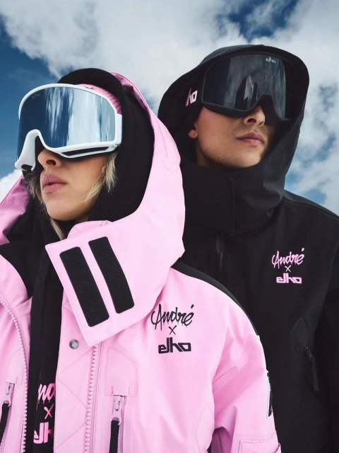 Two fashion models in ski jackets and goggles pose against a cloudy sky, showcasing winter sports and outdoor apparel.