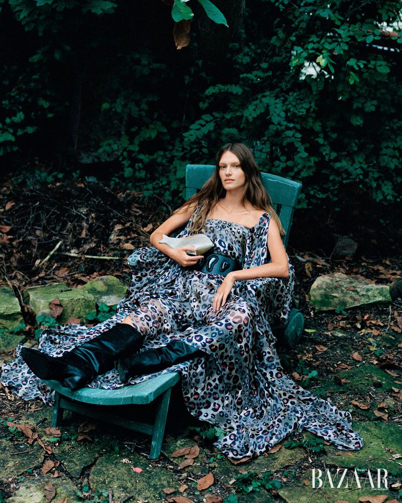 Model wearing a patterned dress and black boots seated in a garden chair outdoors