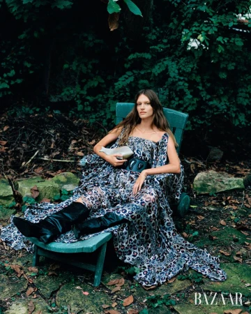 Model wearing a patterned dress and black boots seated in a garden chair outdoors