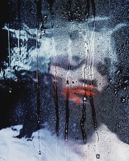 Abstract image of an adult female with red lips, obscured by water droplets on glass, creating a distorted and artistic portrait.