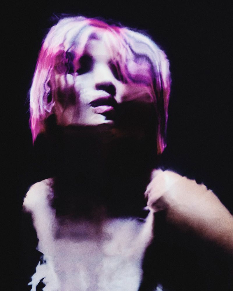 Abstract portrait of an adult woman with pink and white hair against a dark background with a blurred effect.