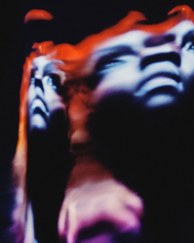 Artistic portrait of a woman with red hair against a dark background, creating a mysterious and abstract visual.