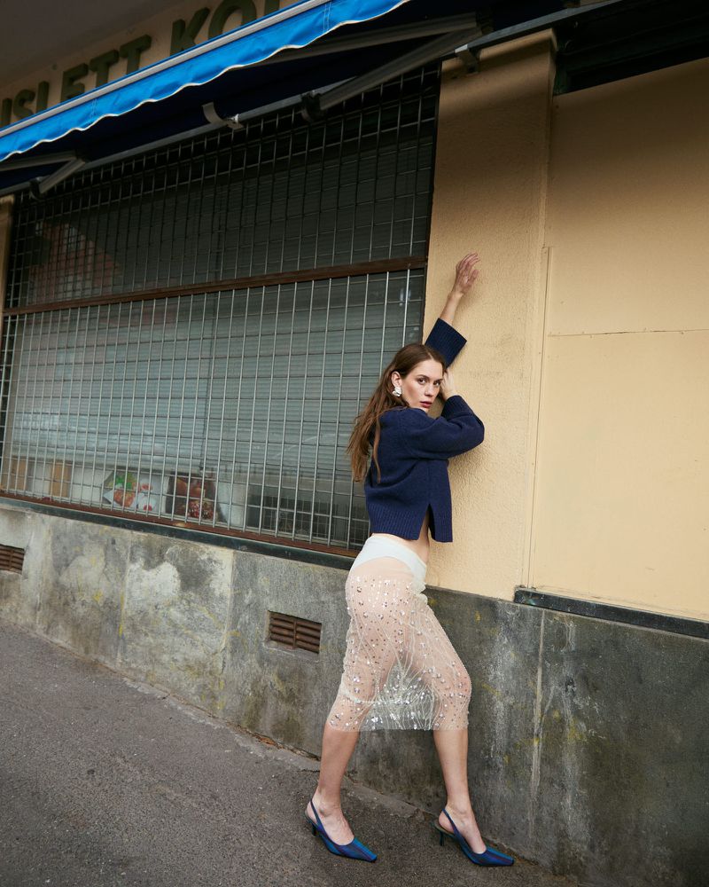 Adult woman posing on an urban street wearing a cropped dark blue jacket and sheer skirt with pumps.