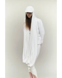 Model in an all-white outfit featuring a long draped hood and cap against a neutral background.