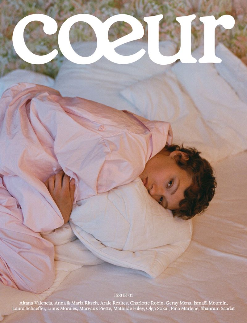 Magazine cover featuring a young adult in pink pajamas reclining against a white pillow on a white bedsheet, with 'coœur' in bold white text.