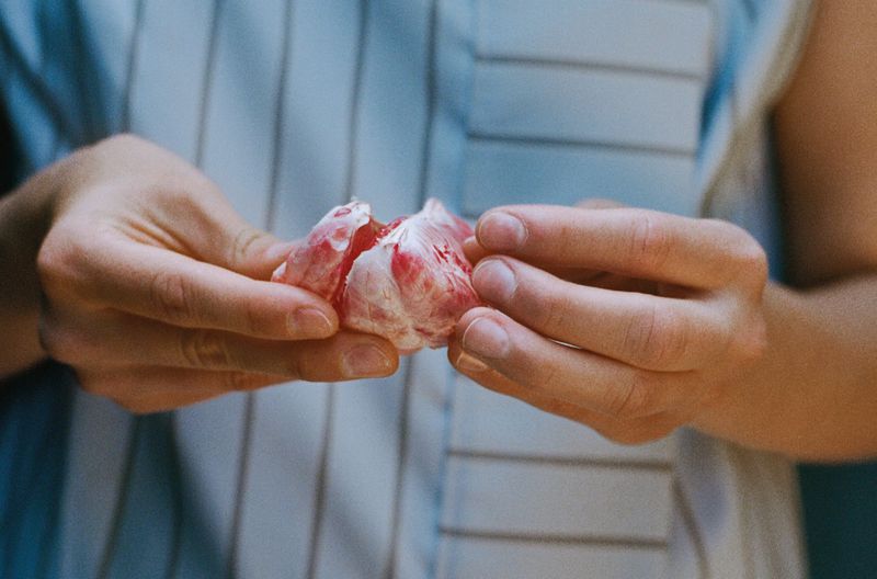 Close-up of hands peeling sections of a red grapefruit, exposing juicy segments. The person wears a striped shirt.