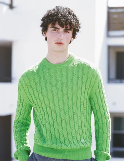 Model Xavier Karwas wearing a bright green cable-knit sweater outdoors in front of a white building for Pop Magazine.