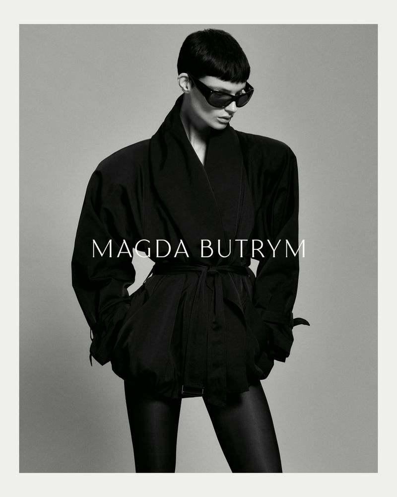 A stylish woman wearing a black jacket and sunglasses poses against a grey background. The image includes text 'MAGDA BUTRYM'.