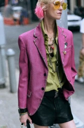 Model with dyed pink hair wearing a magenta blazer and yellow sunglasses standing outdoors