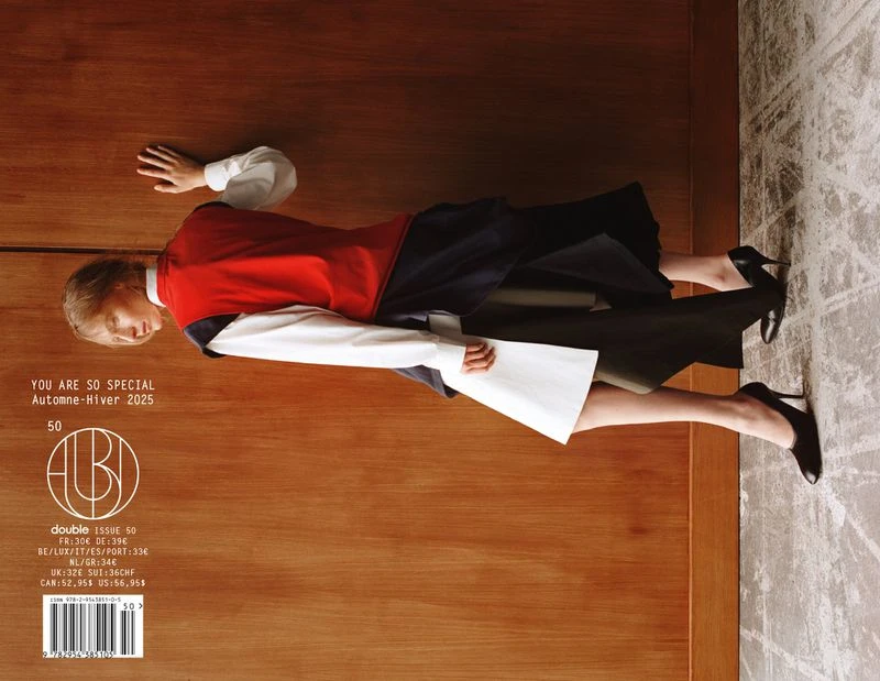 Fashion magazine cover featuring a woman in modern clothing, lying diagonally on a wooden surface against a textured background.