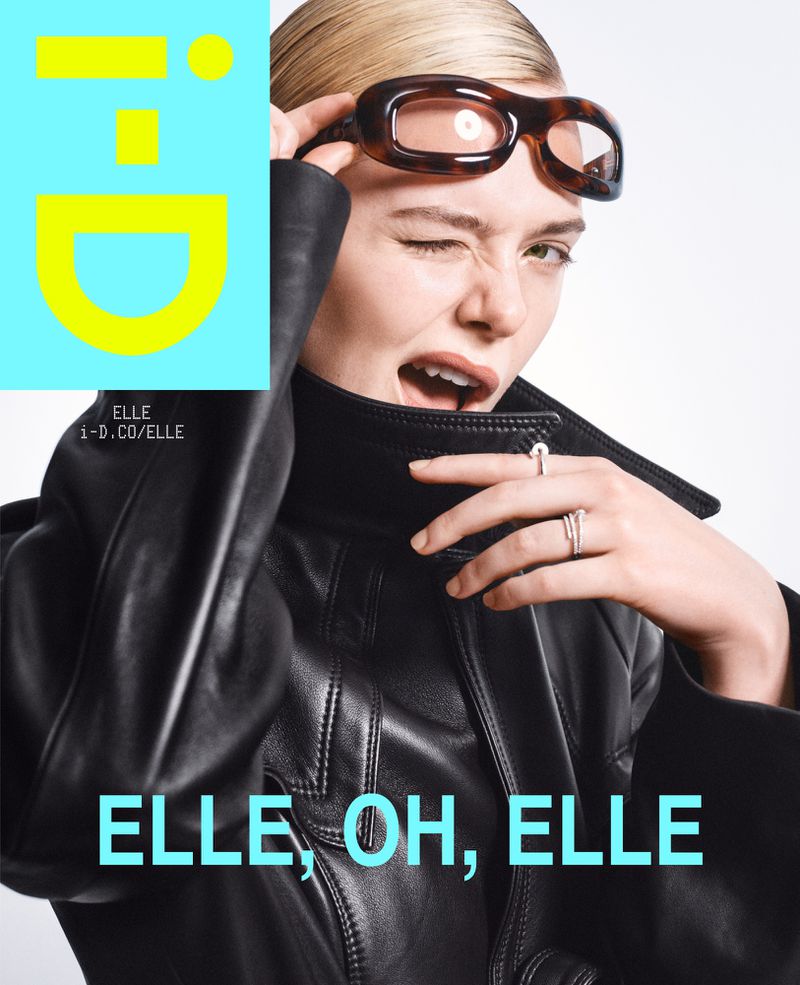 Portrait of a blonde woman wearing sunglasses and a black leather jacket, winking, in front of a magazine cover with blue and yellow graphic.