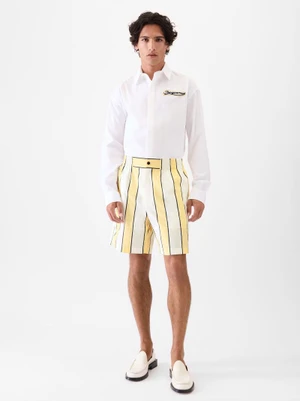 Model Morgan Sahadow in a white shirt, yellow-striped shorts, and white loafers against a white studio background.