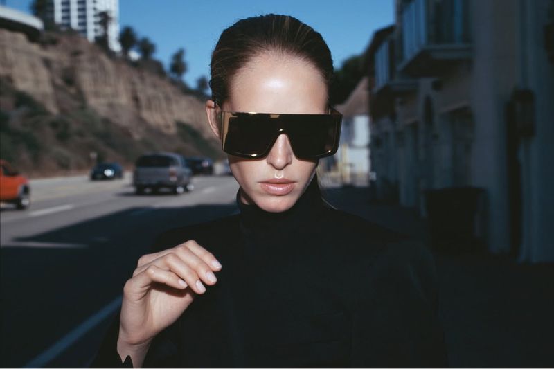 Model Abby Champion wearing dark oversized sunglasses and black clothing outdoors on a street for Double Magazine.