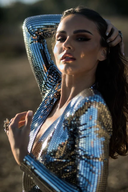 Attractive woman in a shiny, sequined silver dress posing outdoors with a blurred background, showing fashion and style.