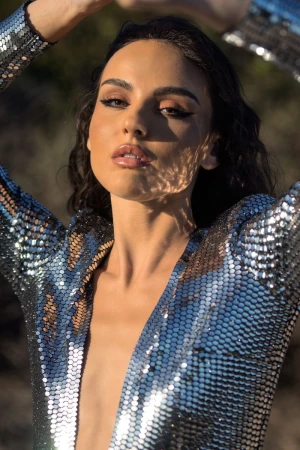 Close-up portrait of a woman wearing a shimmering silver sequin top with her arms raised