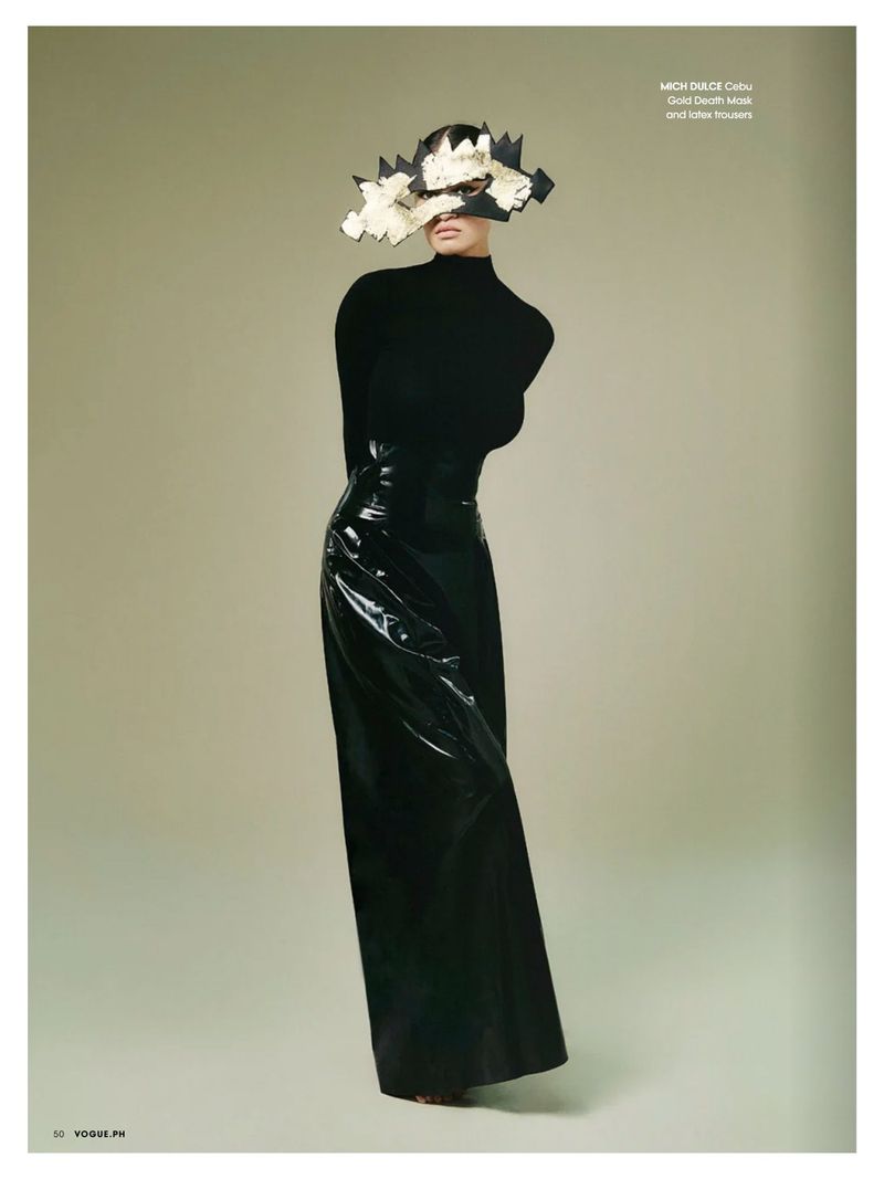 Fashion editorial shot featuring an adult female model in a black turtleneck and glossy skirt with a floral hat against a beige background.