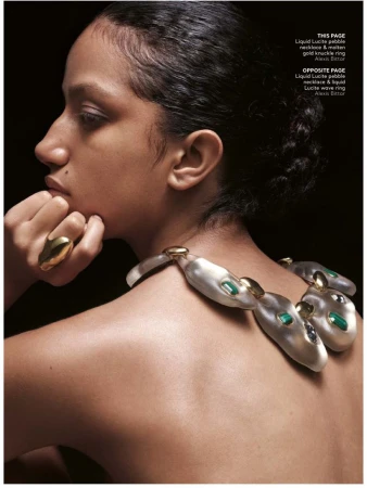 An adult female model poses in a studio with dramatic lighting wearing a necklace and ring, showcasing fashion jewellery on a dark background.