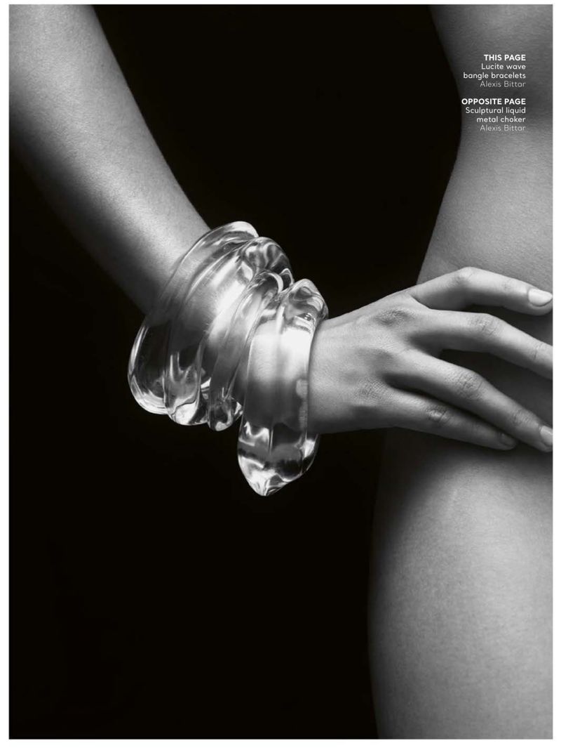 Close-up studio shot of a woman's arm adorned with chunky, clear Lucite bangle bracelets against a stark black backdrop, fashion editorial.