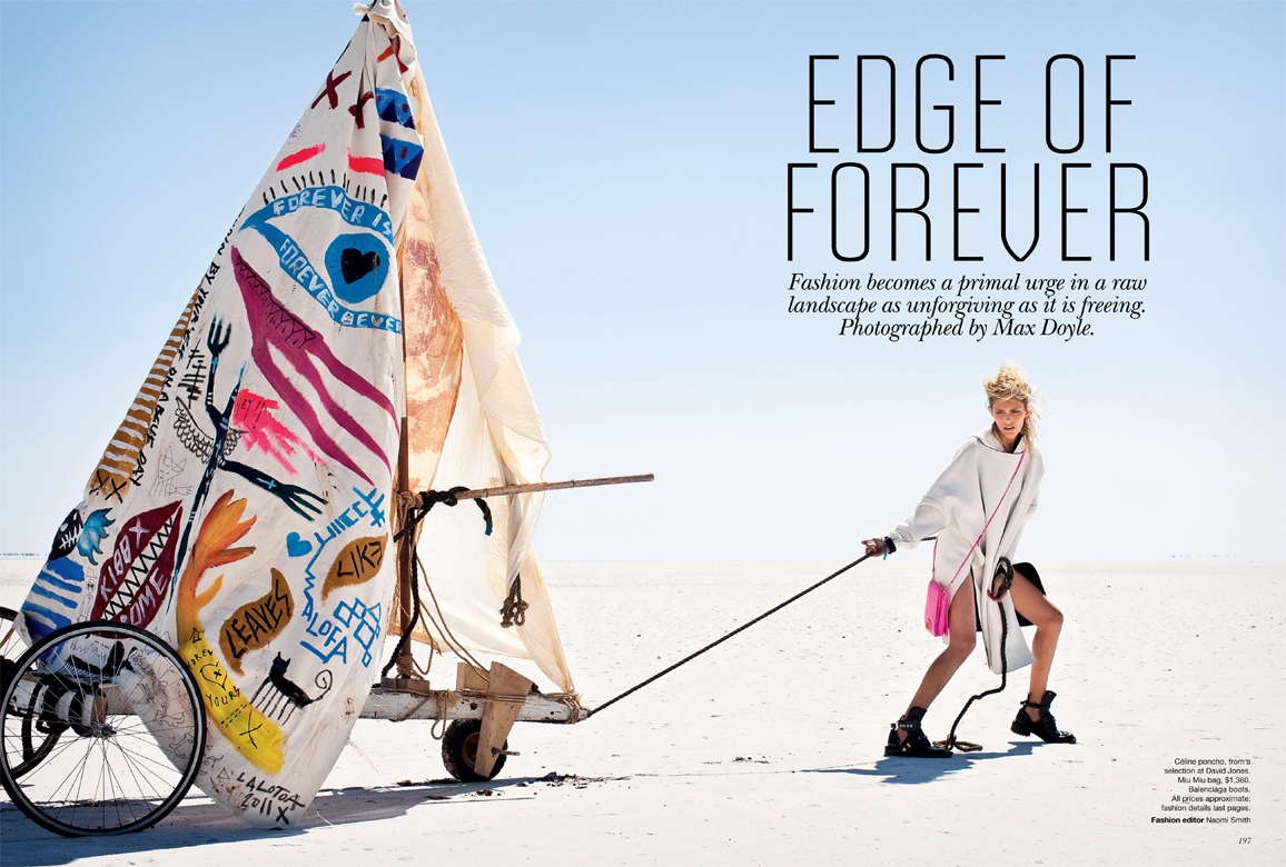 Fashion shot of a woman in a hooded outfit pulling a sail-cart on a salt flat under a bright sky, featuring hand-painted graphics.