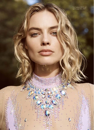 Close-up of a woman with blonde wavy hair wearing an embellished lavender dress, posing outdoors with natural light, looking directly at the camera.
