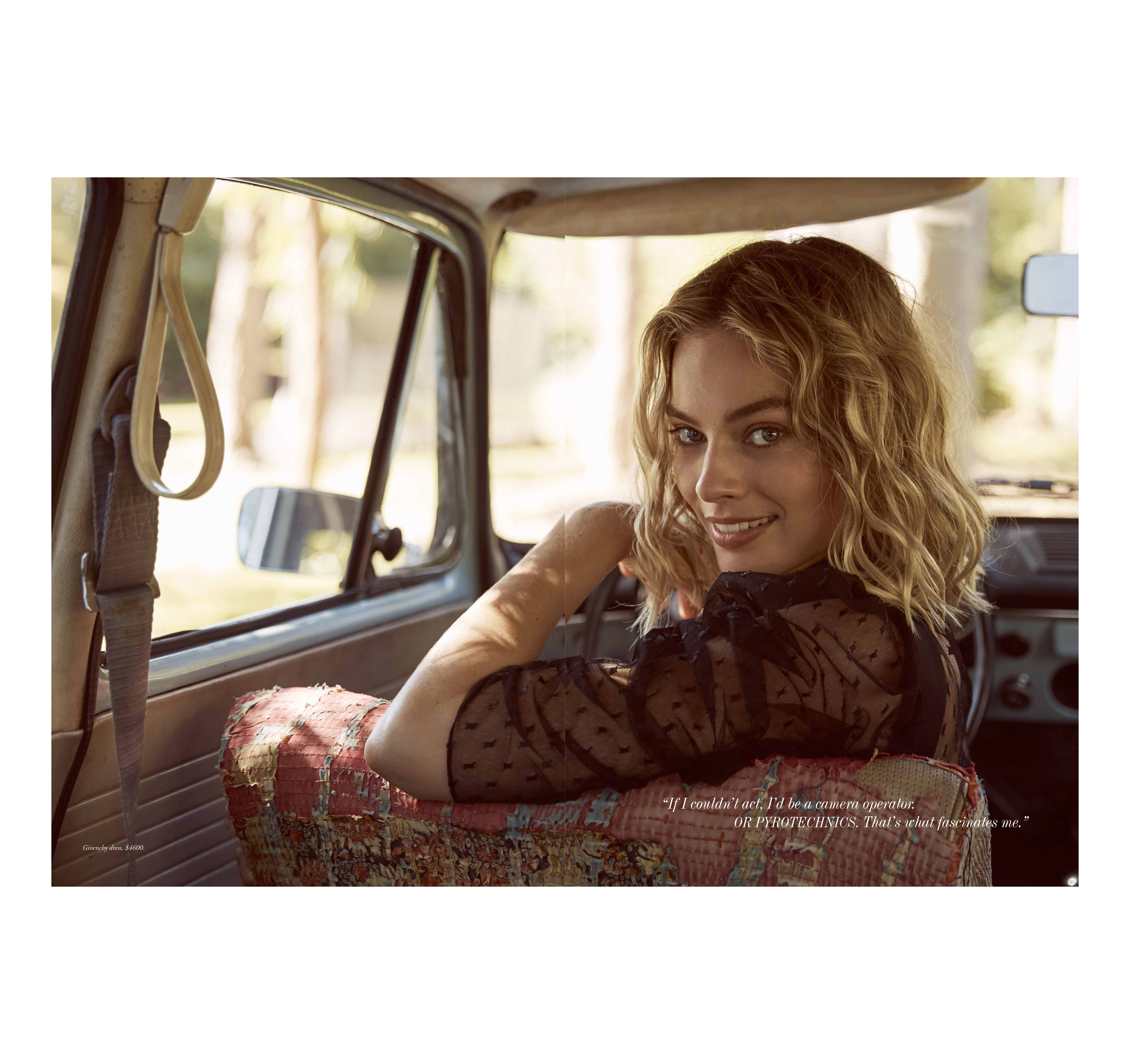 Woman in car smiles, wearing sheer black top, wavy blonde hair, sitting in patterned car seat with sunny trees blurred behind.
