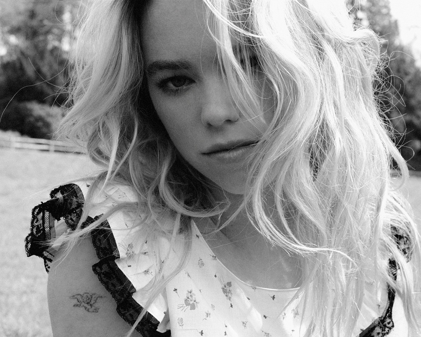Black and white portrait of a blonde woman wearing a floral-patterned top with black lace accents, captured outdoors in natural light.