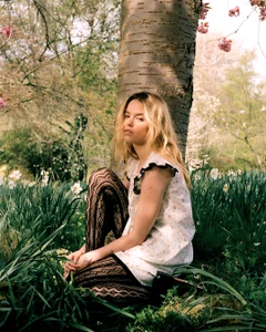 Milly Alcock crouching against a large tree trunk in a spring garden with blooming flowers for Elle Australia