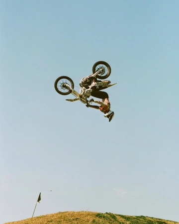 A motocross rider performs a backflip mid-air with a motorcycle against a clear sky, showcasing skill and precision in action sports.