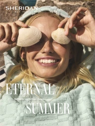 Close-up portrait of a smiling blonde woman holding seashells over her eyes, wearing a mint green hooded towel robe.
