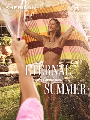 Smiling woman holding a striped beach towel outdoors as water splashes around her in sunlight