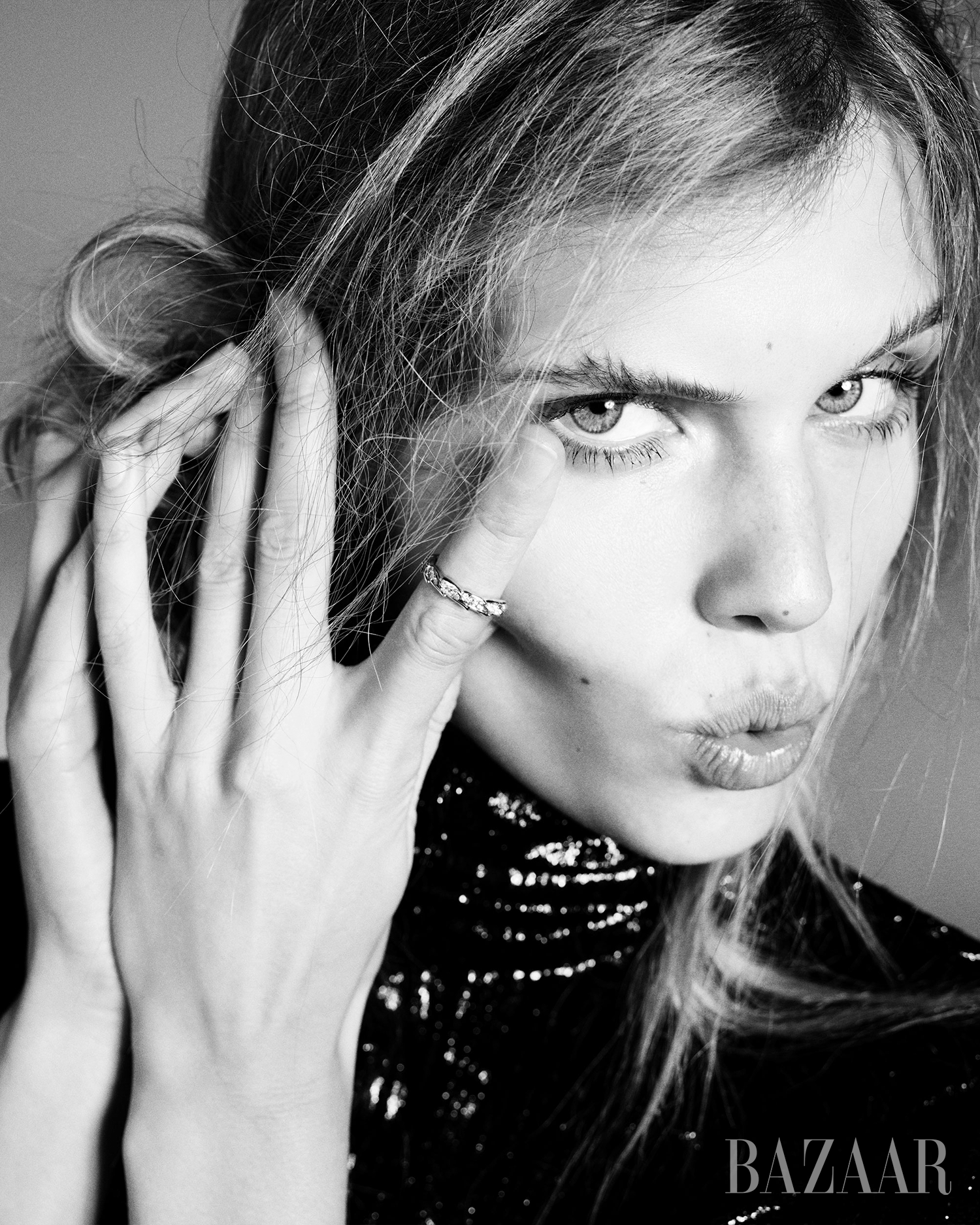 Black-and-white portrait of a woman with fair skin, light hair, wearing a sequined top and ring on her finger, with a neutral background.