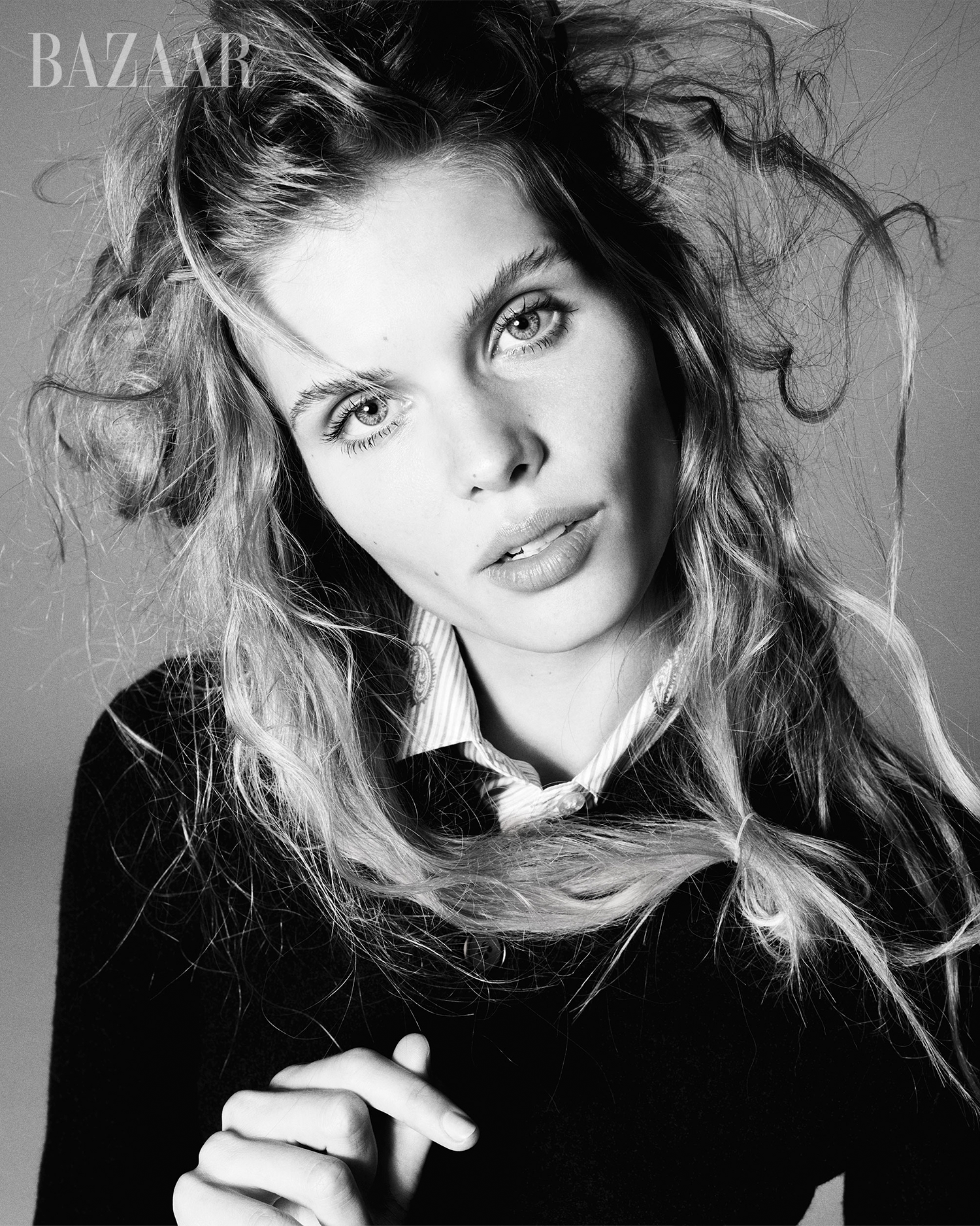 Black and white portrait of a fair-skinned adult female model with wavy blonde hair, wearing a dark top and collared shirt.