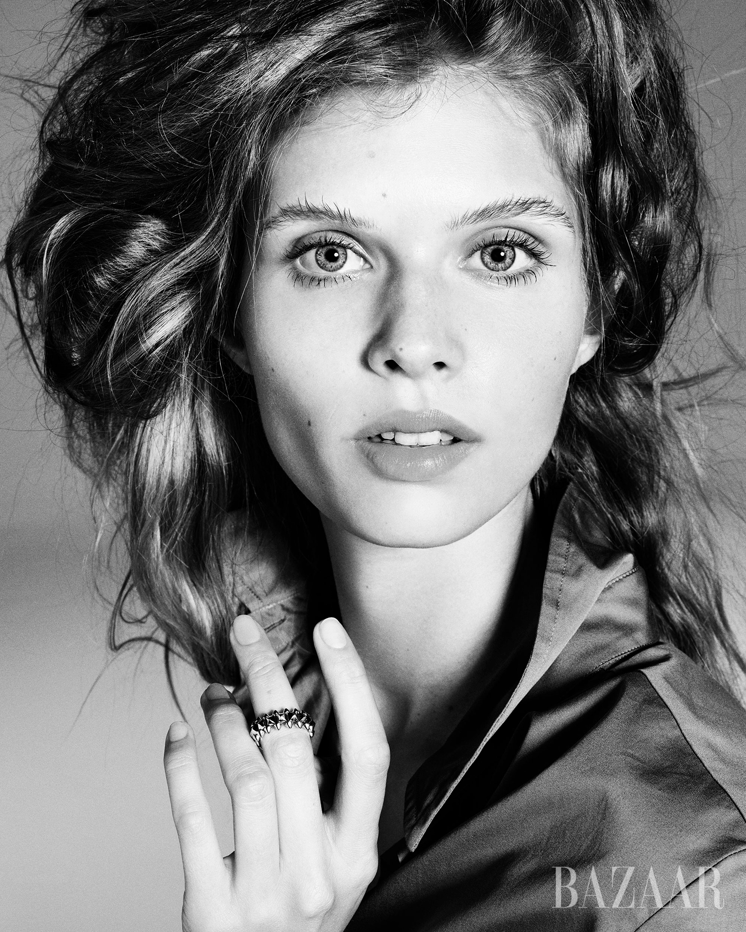 Striking black and white beauty portrait of a young adult female model with wavy hair, wearing a ring, captured in a photo studio.