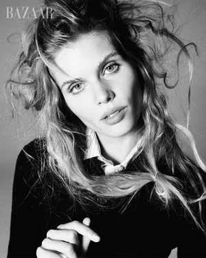 Black and white portrait of model Ida Heiner with tousled hair wearing a dark cardigan and collared shirt against a grey background.