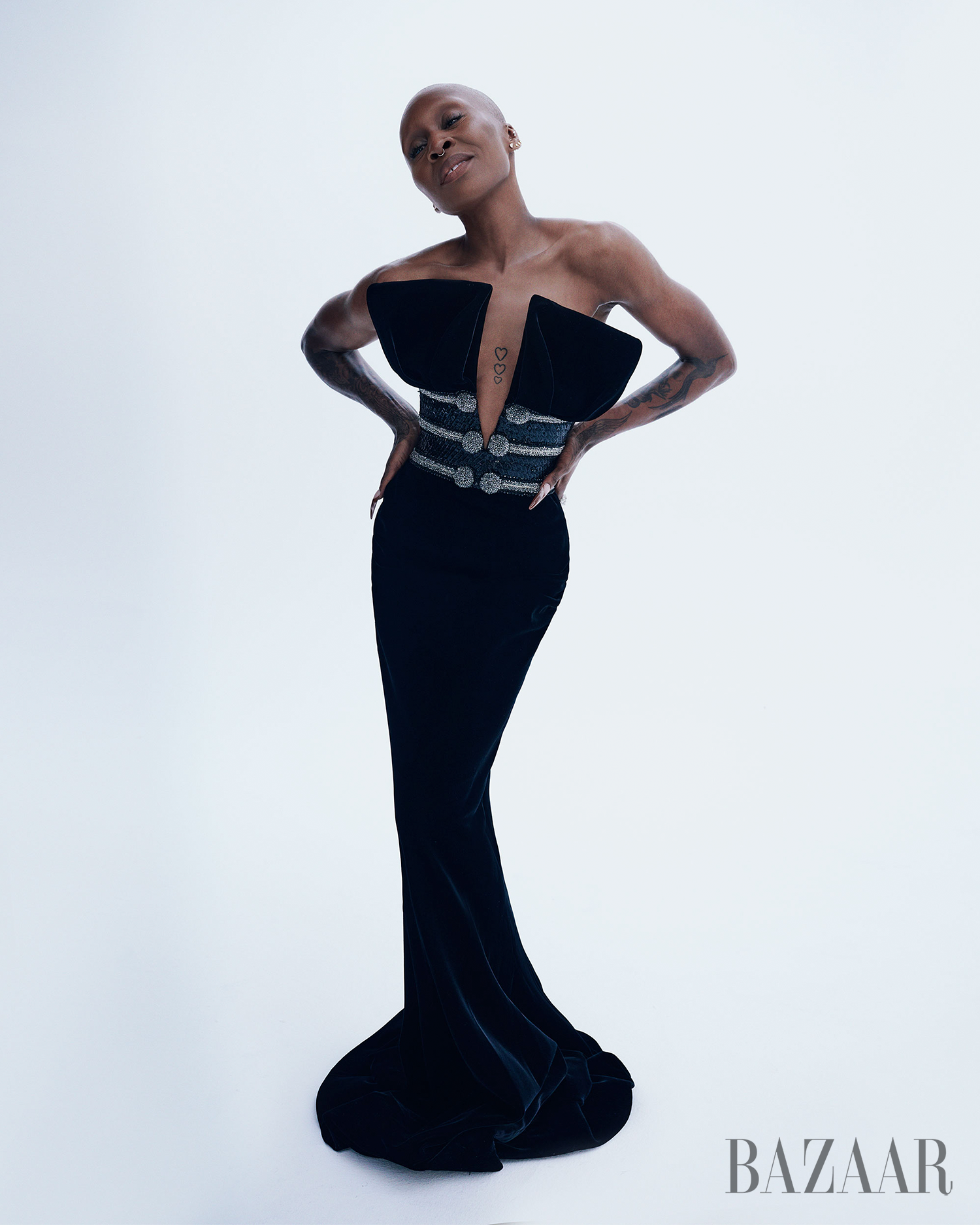 A striking fashion portrait of a Black woman in a black velvet dress with a decorative belt, confidently posed against a white backdrop.