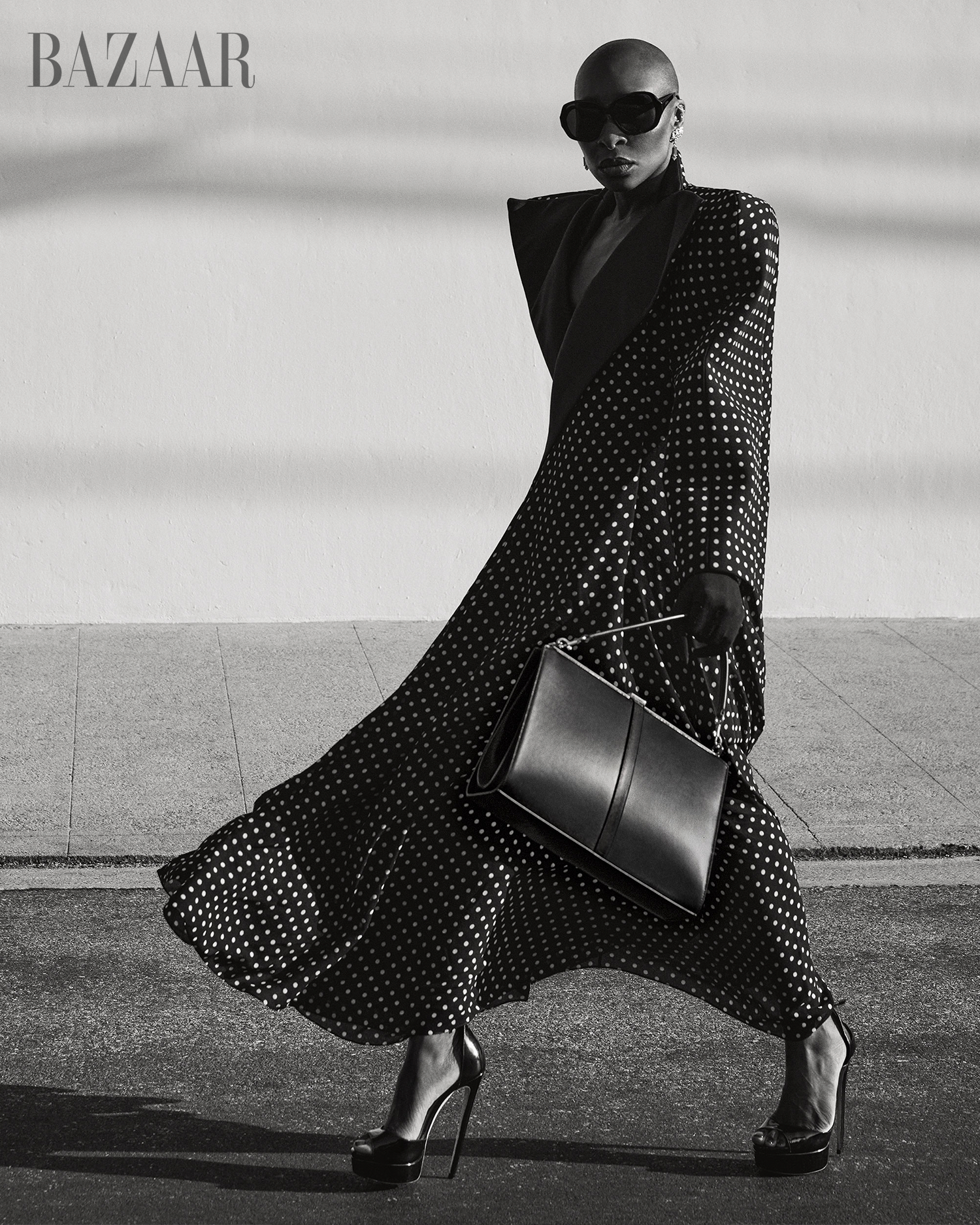 Cynthia Erivo wearing polka-dot coat and sunglasses holding a black handbag in black and white fashion editorial