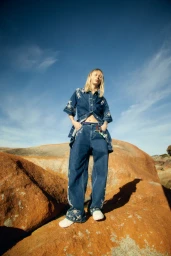 Model standing on red rock formations wearing embroidered denim matching set under a bright blue sky.