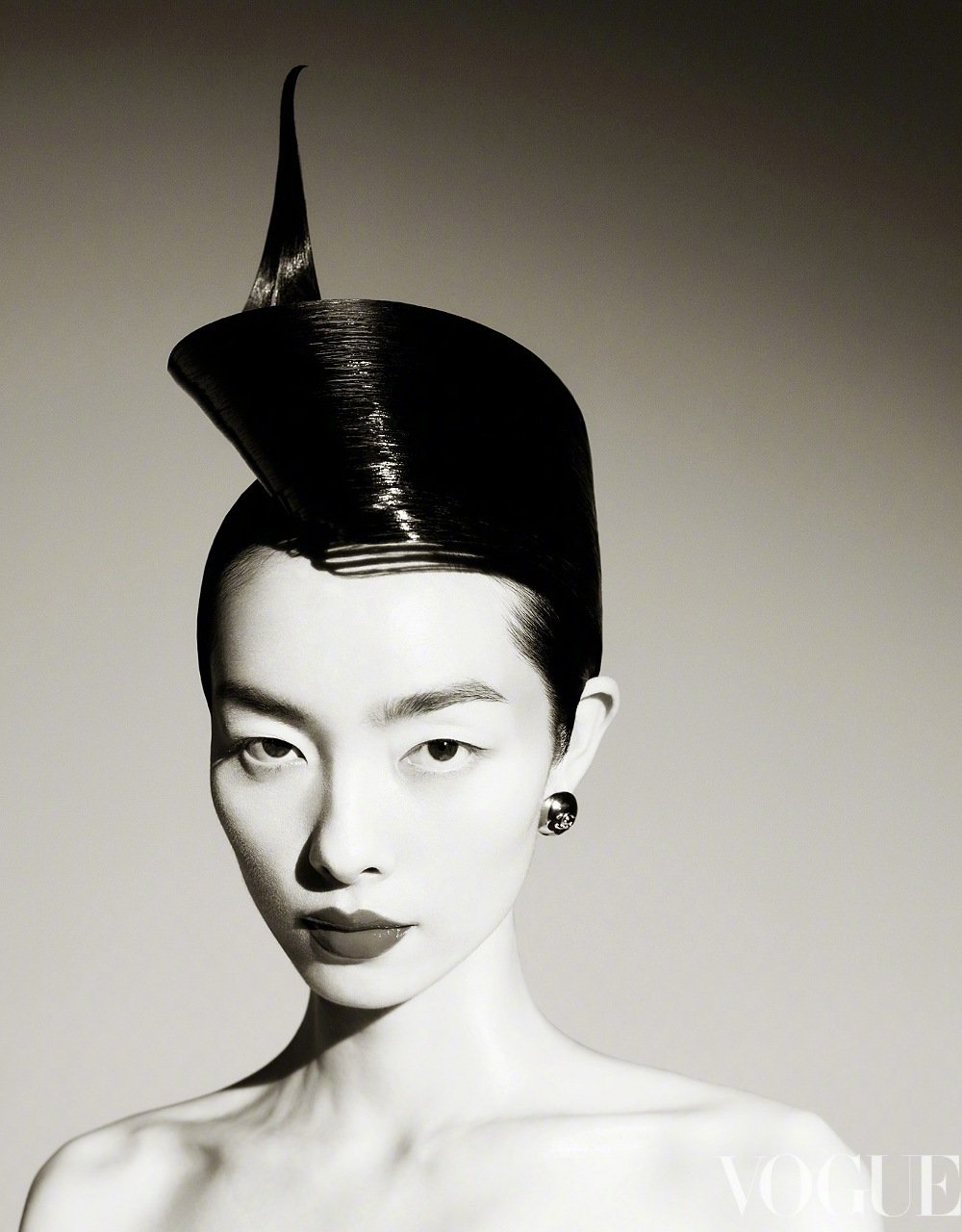 Striking black and white portrait of an Asian woman with unique black sculptural hairstyle, dark lipstick, and stud earrings, Vogue logo visible.