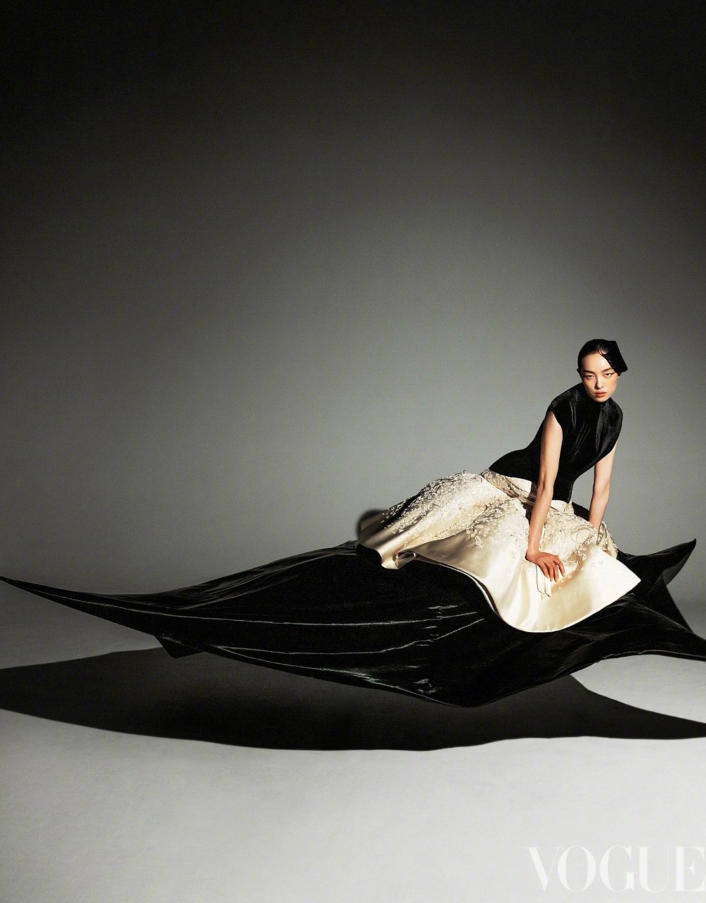 Elegant woman in black and white gown poses dynamically in a fashion studio. Long dress trains trail, studio lighting.