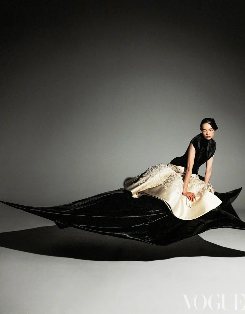 Elegant woman in black and white gown poses dynamically in a fashion studio. Long dress trains trail, studio lighting.