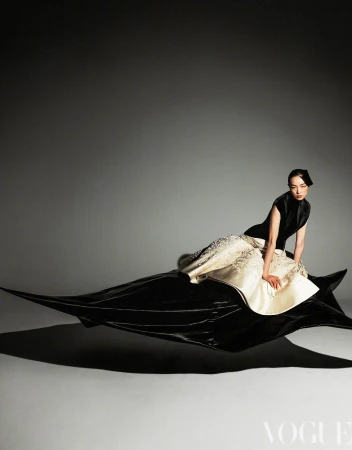 Elegant woman in black and white gown poses dynamically in a fashion studio. Long dress trains trail, studio lighting.