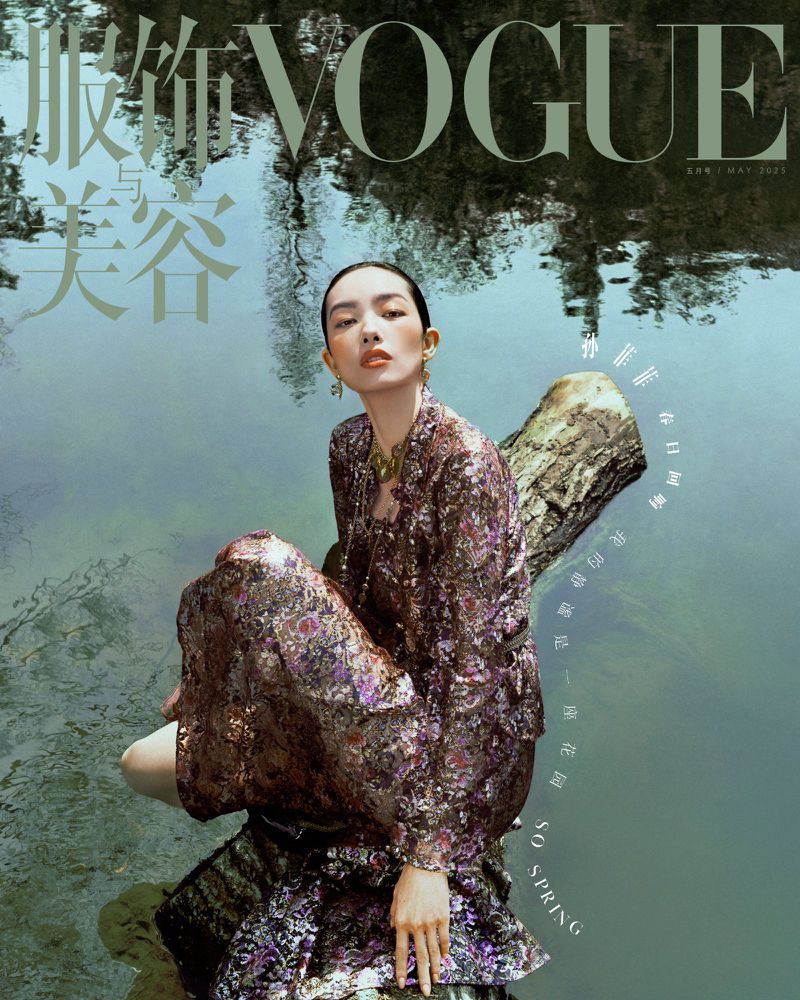Vogue cover featuring a woman in a floral patterned outfit seated on a log in a pond, reflecting trees, creating a natural, serene fashion image.