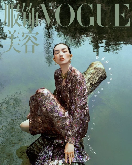 Vogue cover featuring a woman in a floral patterned outfit seated on a log in a pond, reflecting trees, creating a natural, serene fashion image.