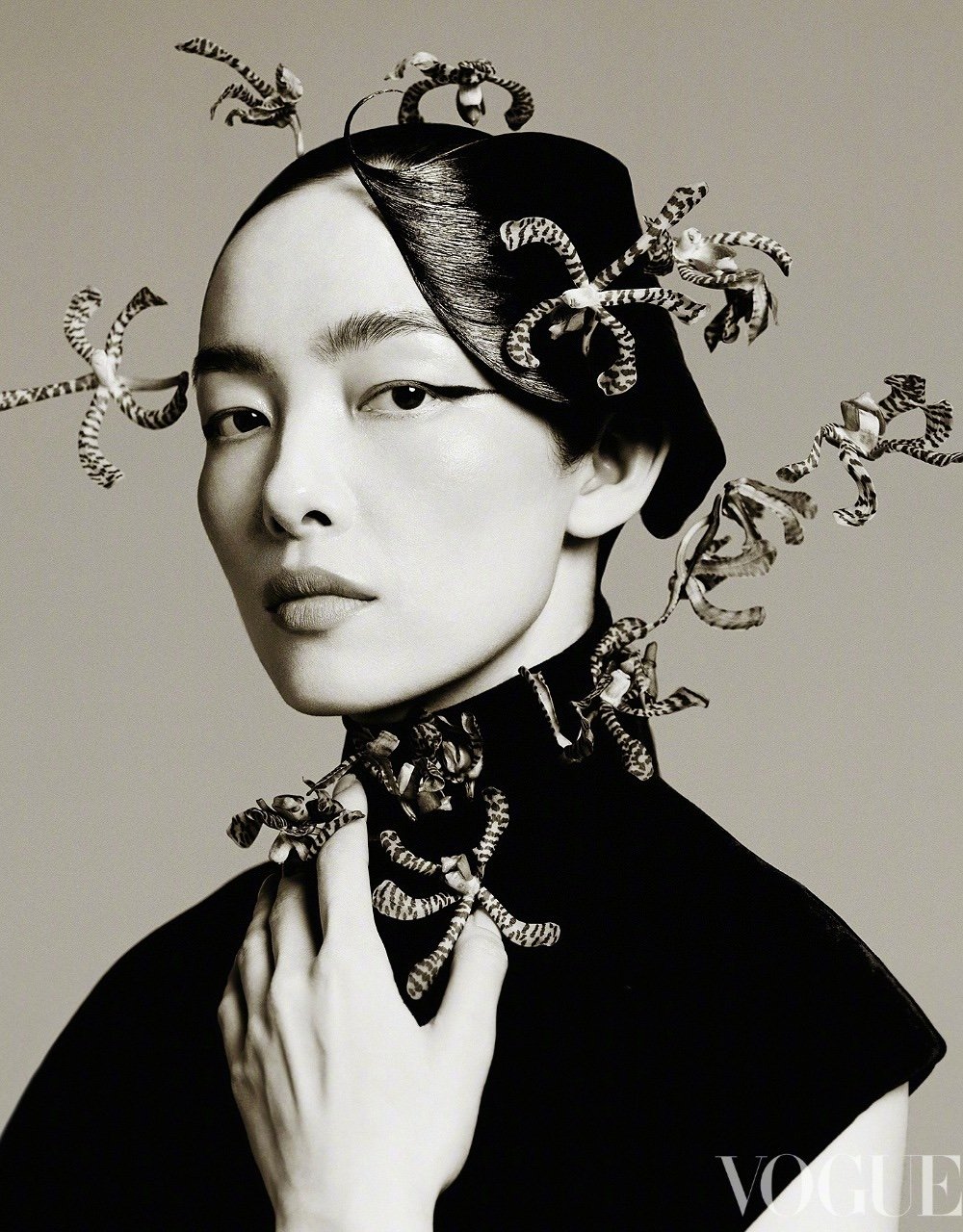 Headshot of an Asian woman wearing a black turtleneck and decorative head and neck piece posing in a photo studio against a grey backdrop.